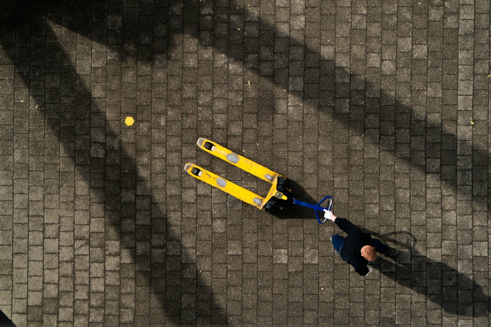 Aerial view of a worker pulling a yellow pallet jack across a paved yard